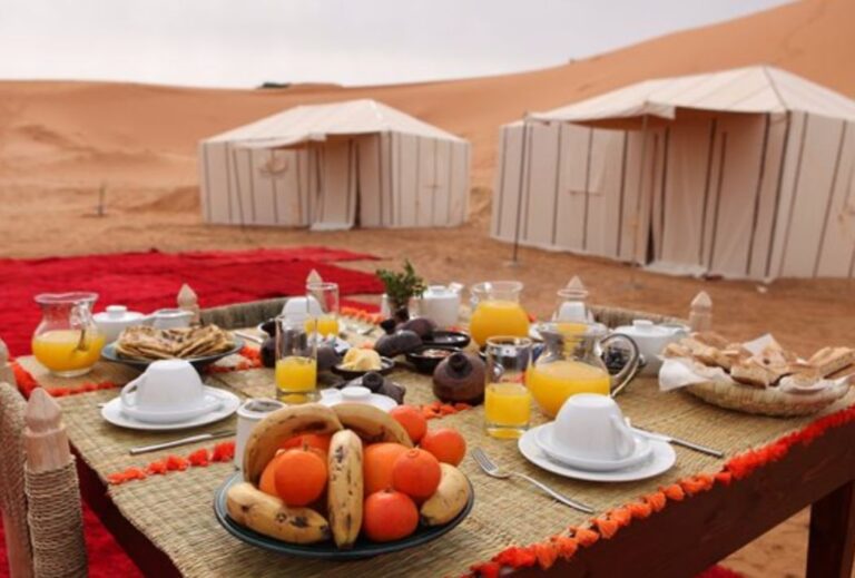 Breakfast served outdoors beside desert camp tents and sand dunes